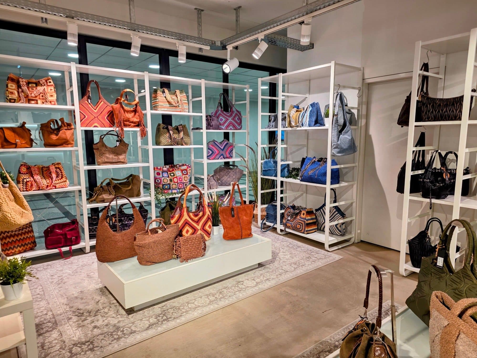 Blick in den Showroom: weiße Regale mit gehäkelten und geflochtenen Taschen in Orange und Rost, daneben Wildleder, Denim und Schwarz. Im Vordergrund ein Podest mit Raffia-Shoppern.